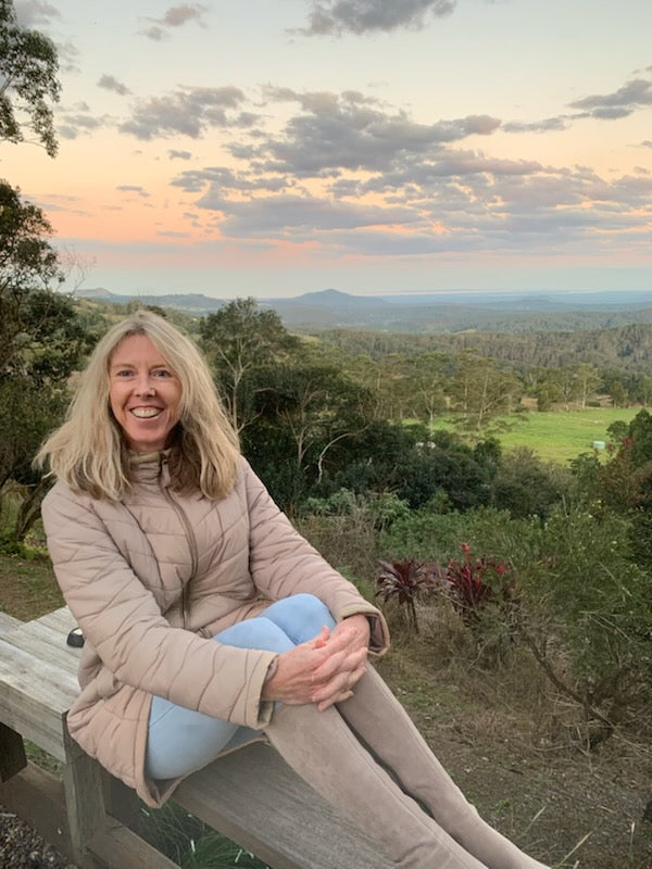 Photo of Dr Rachel Sawyer smiling and sitting on a bench with mountain and bush landscape behind her.